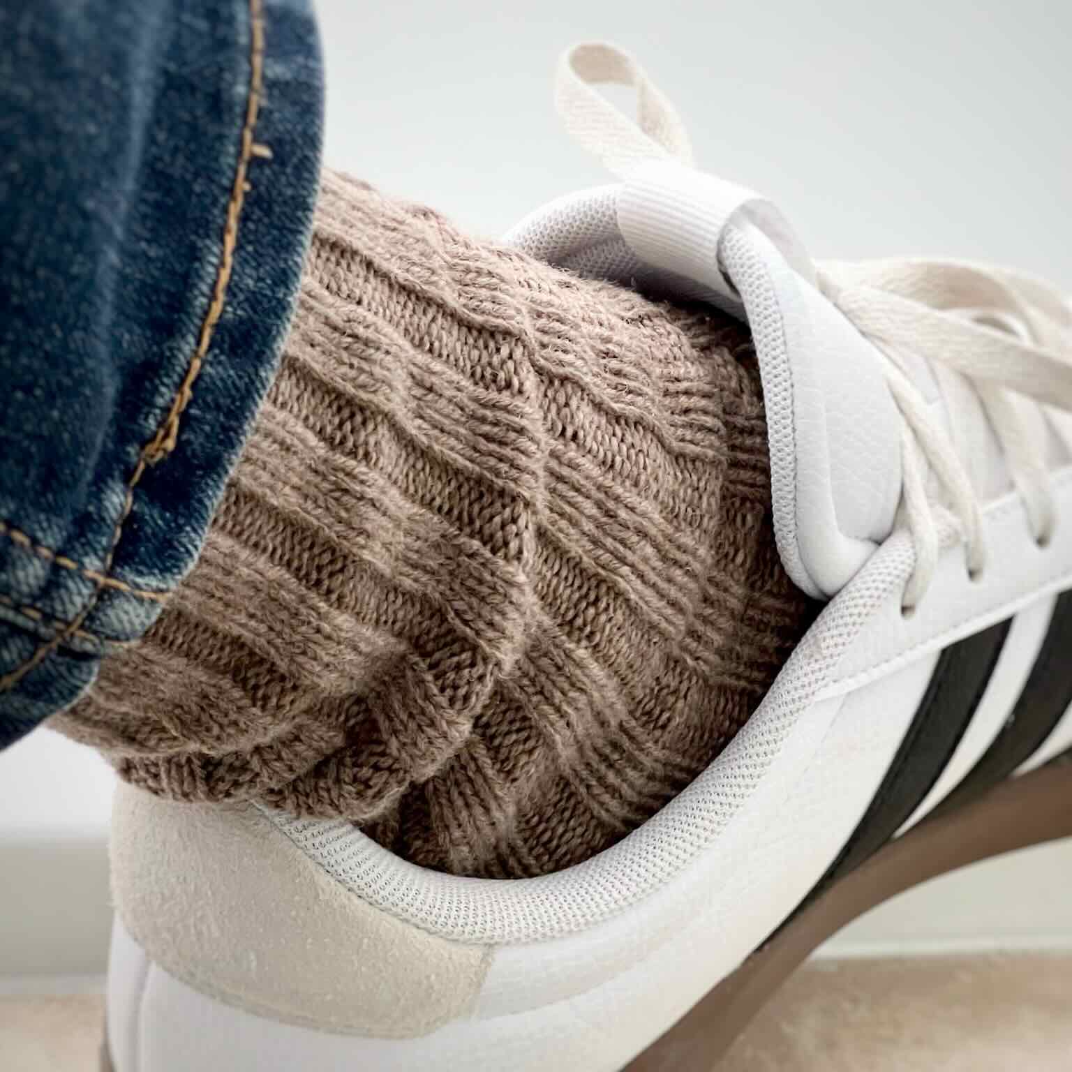 White sneaker with brown ribbed wool sock and blue jeans.